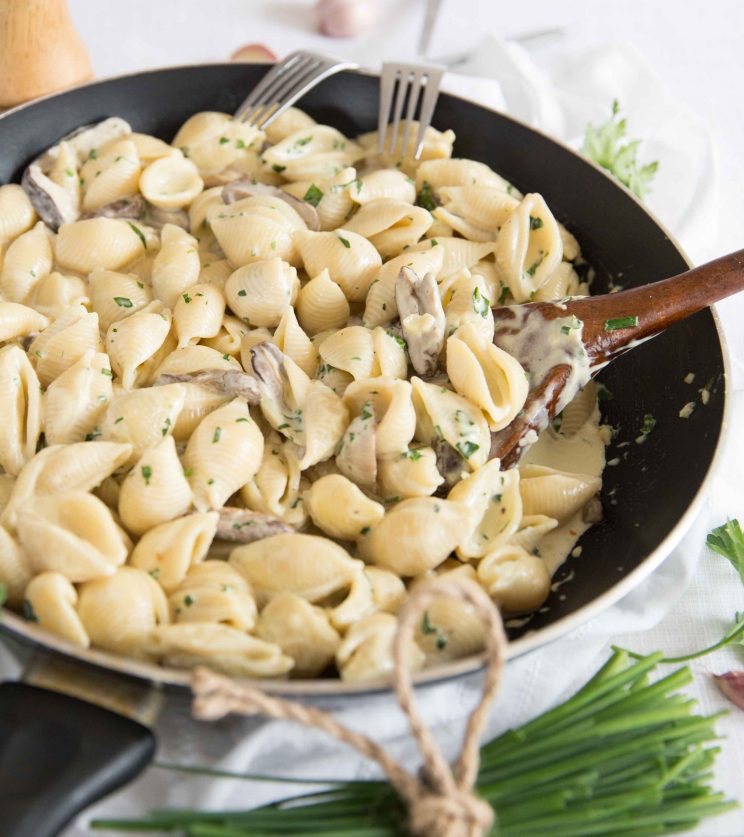 side view shot of creamy mushroom pasta in skillet with wooden spoon digging in