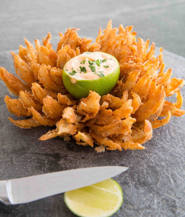 blooming onion on slate with lime dip in the centre and knife blurred in front