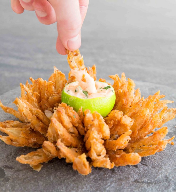 close up shot of hand dunking onion petal into dip in blooming onion