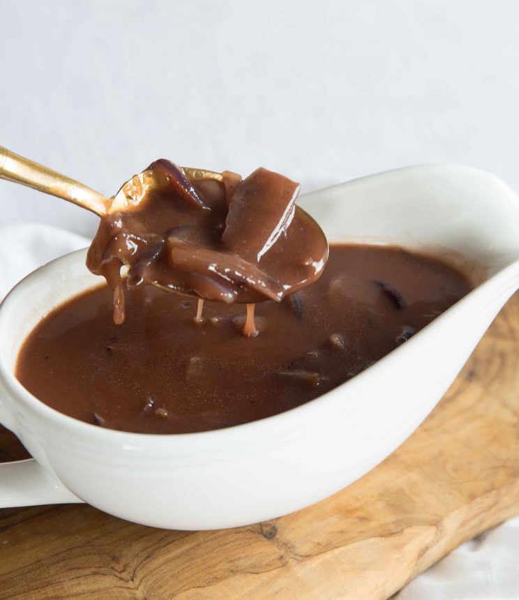 golden spoon dunking into white gravy boat of red wine onion gravy