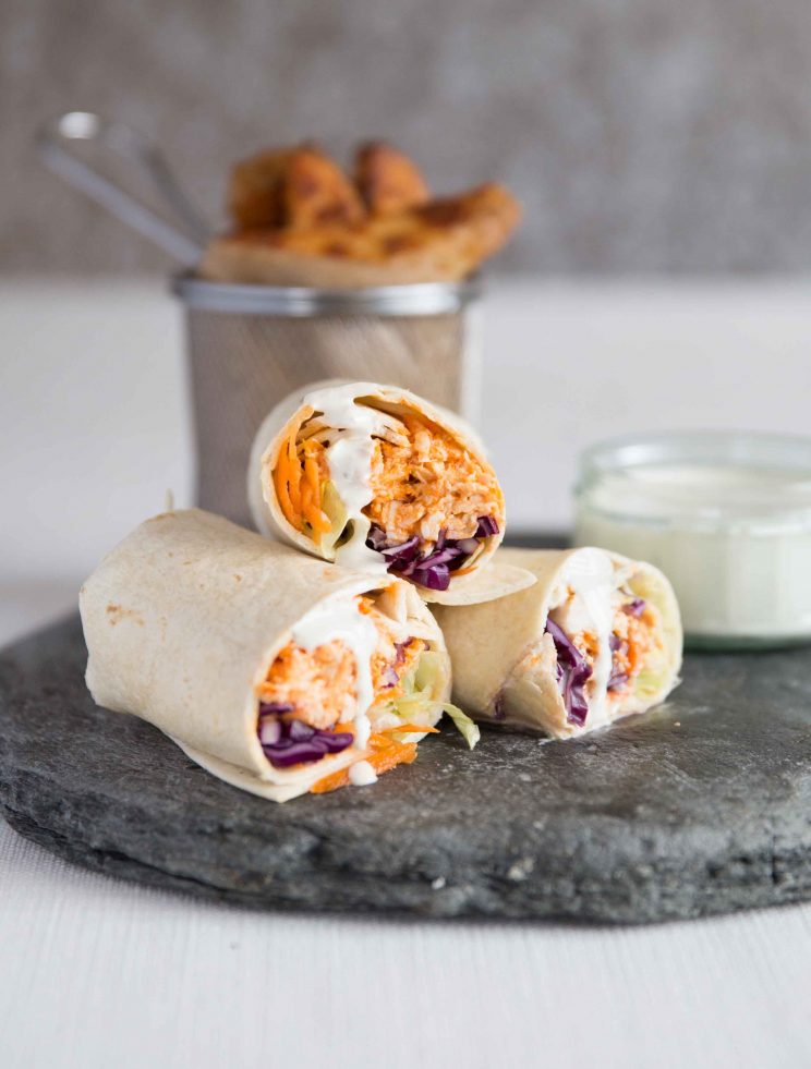 Buffalo Chicken Wraps on slate served with with blue cheese sauce and potato wedges blurred in background