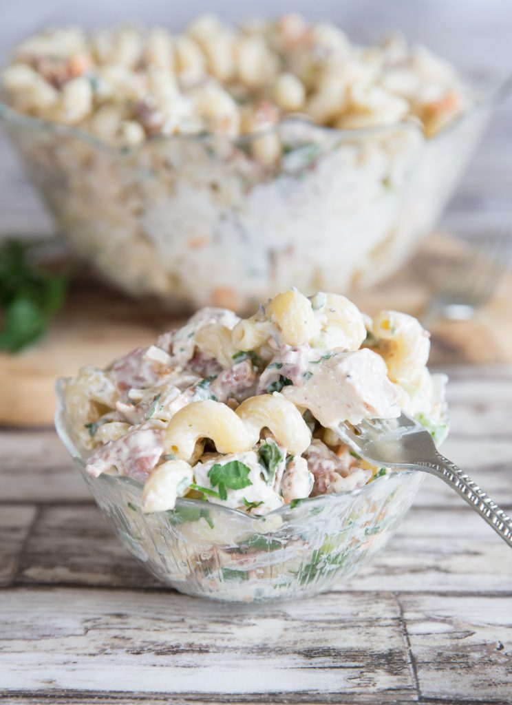 close up shot of pasta salad in small glass bowl with large glass bowl blurred in background