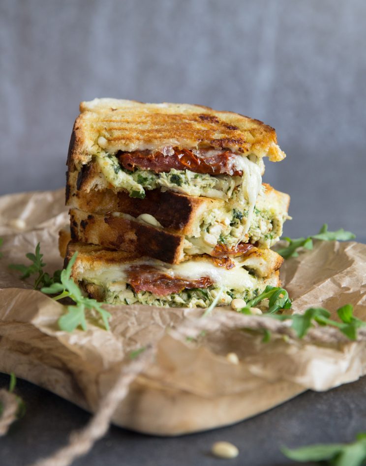 3 sandwich halves stacked on each other on wooden board with mozzarella dripping down