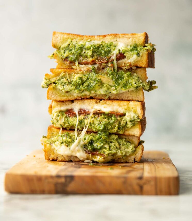 4 sandwich halves stacked on each other on wooden board showing chicken pesto filling