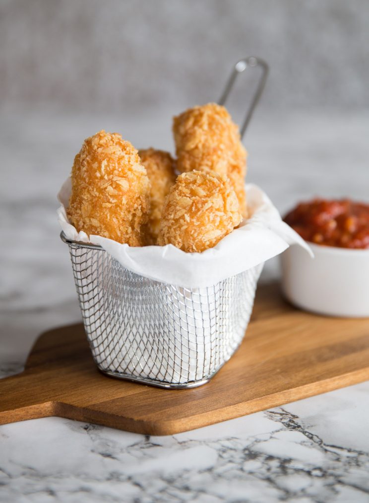 halloumi fries in wire serving pot with marinara dip blurred in background