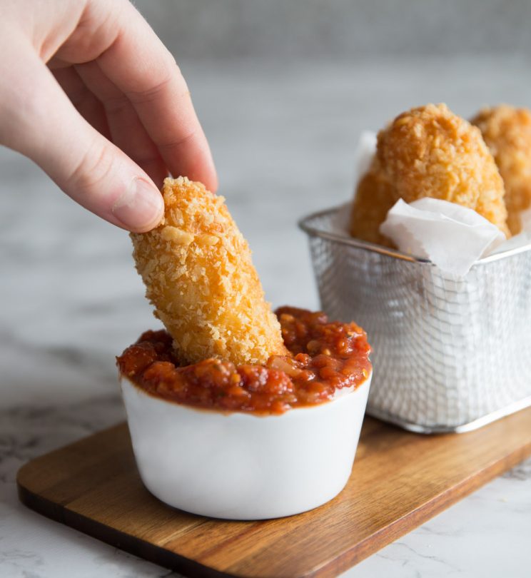 dunking halloumi fry into pot of sauce with more fries blurred in the background