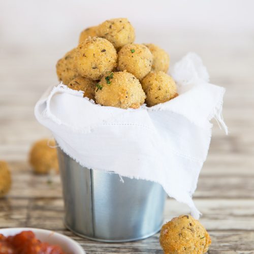 cheese balls served in a tin bucket with marinara dip blurred in the front