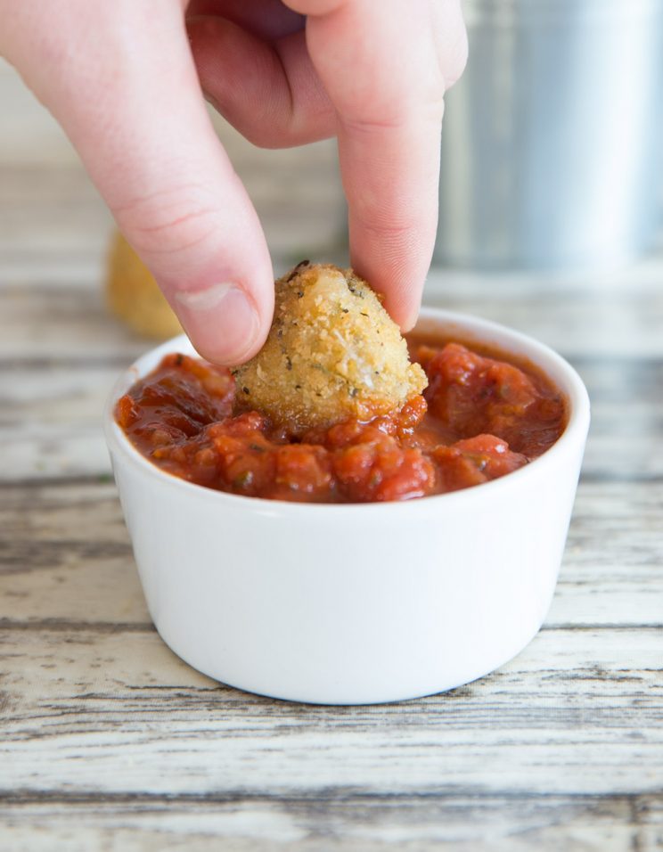 dunking cheese ball into small white pot of marinara dip