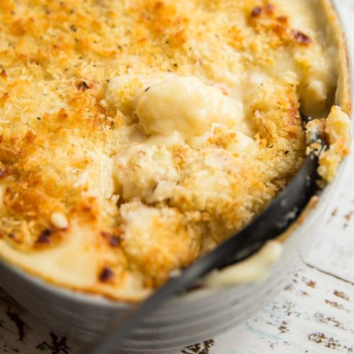 Scooping into baked gnocchi mac and cheese with large black spoon