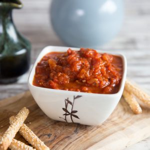 pot of sauce on wooden board with breadsticks blurred in the background