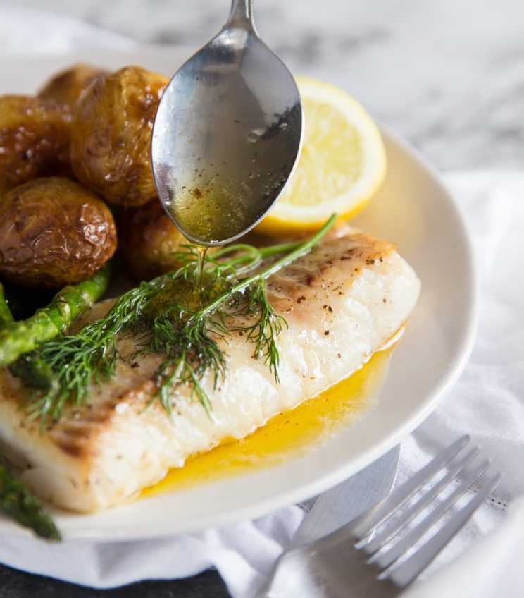 Pan fried cod with brown butter sauce dripping off spoon