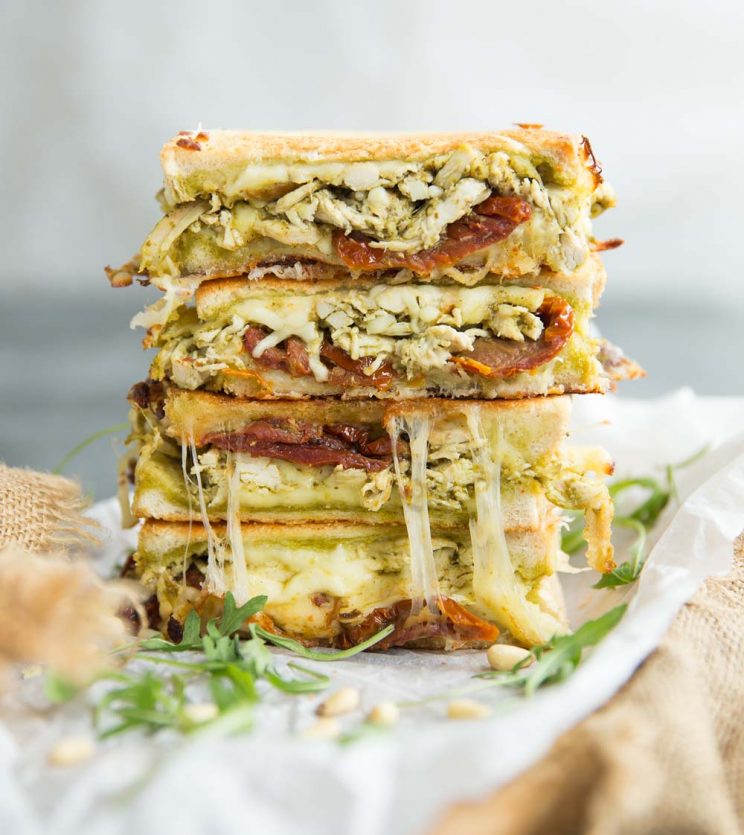 4 slices of Chicken Pesto Grilled Cheese stacked on eachother garnished with arugula and pinenuts