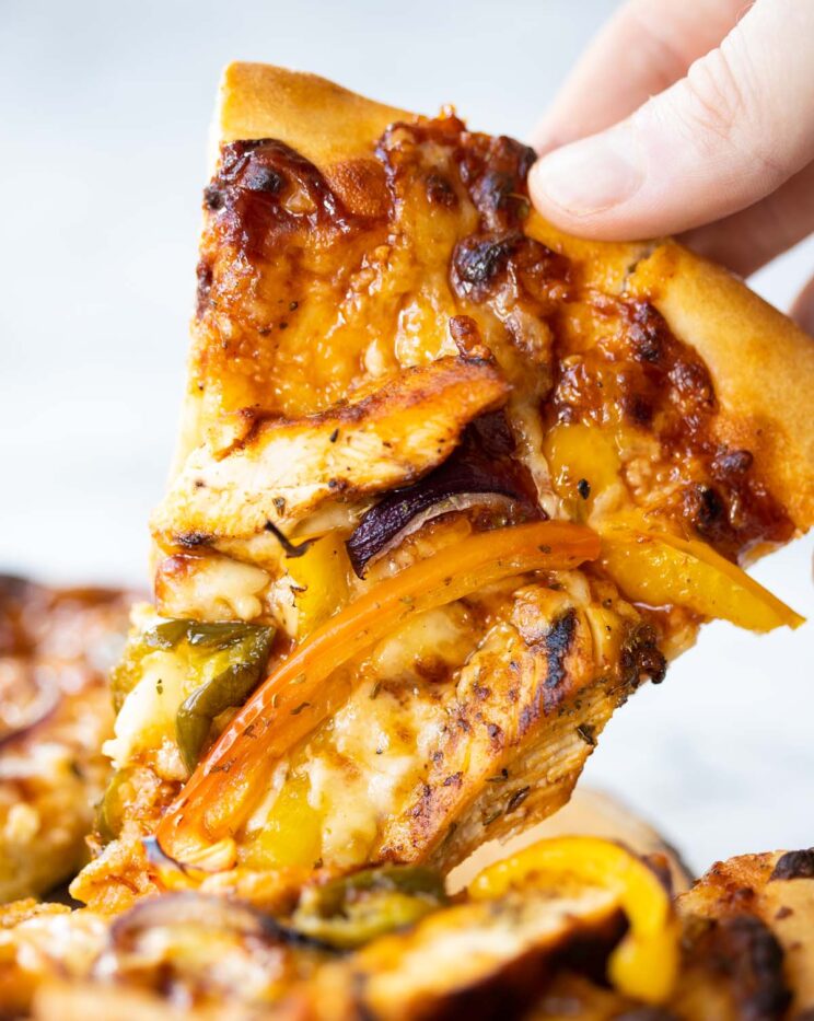 close up shot of hand lifting slice of bbq chicken pizza