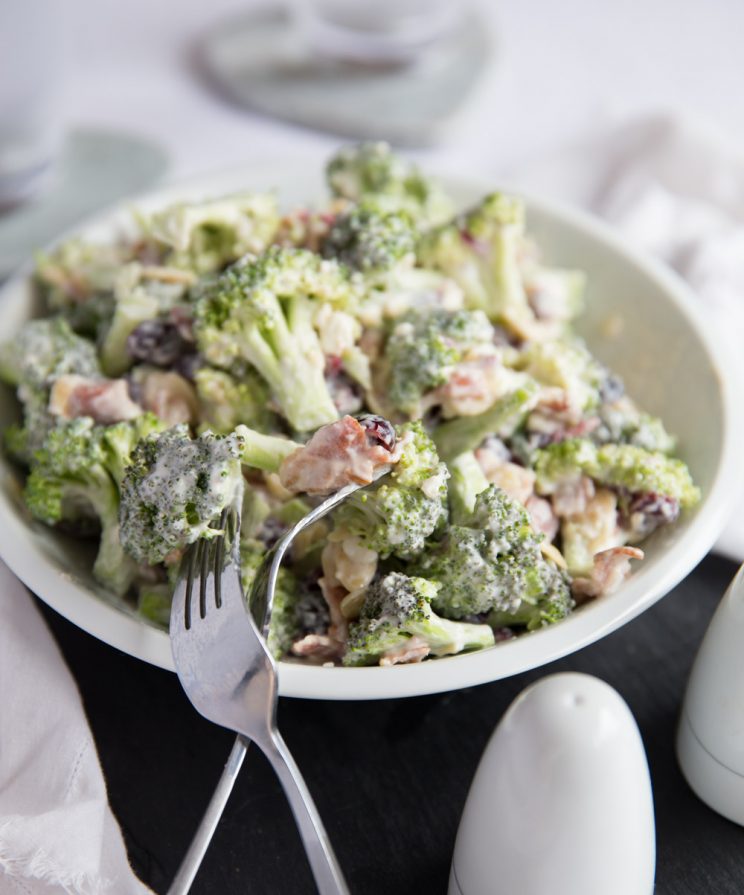 broccoli salad served in white bowl with two silver forks resting on it