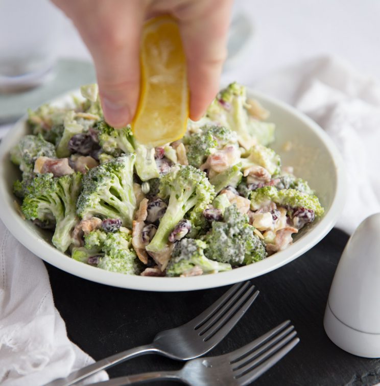 squeezing lemon juice over broccoli salad in white bowl