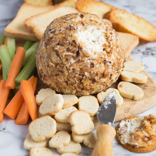 cream cheese ball coated in crispy fried onions on chopping board with biscuits and bread