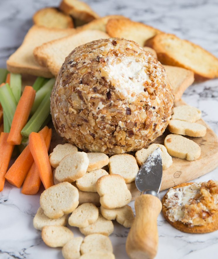 cream cheese ball coated in crispy fried onions on chopping board with biscuits and bread