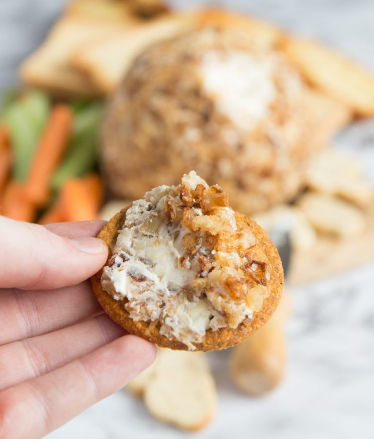 cheese ball spread over a cracker holding to camera with ball blurred in background