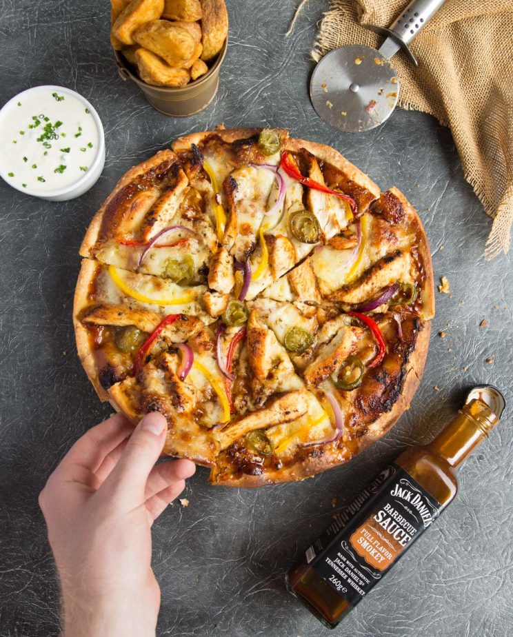 overhead shot of pizza with hand grabbing slice surround by wedges, sauce and dip