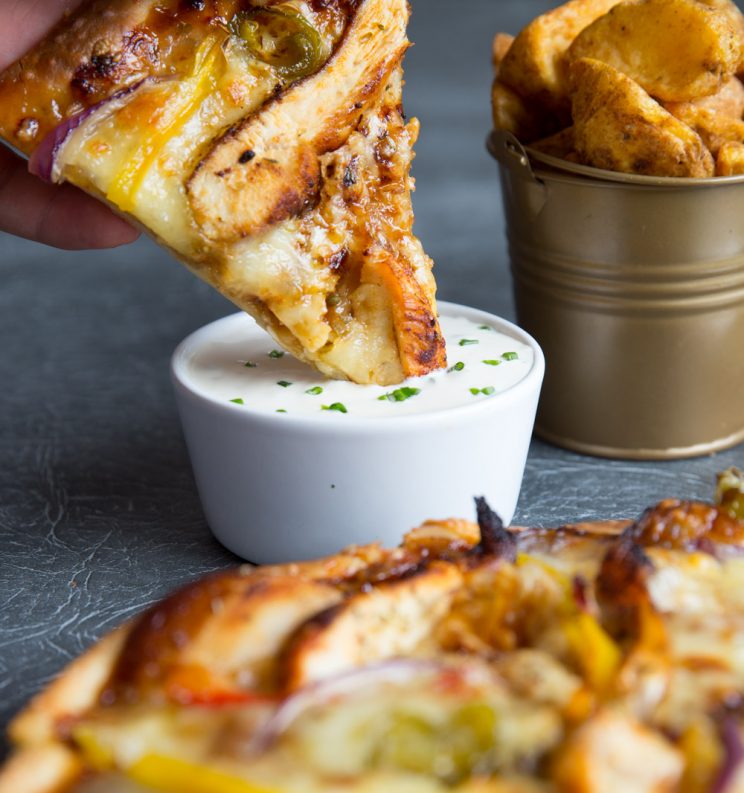 Smoky BBQ Chicken Pizza being dunked into pot of dip