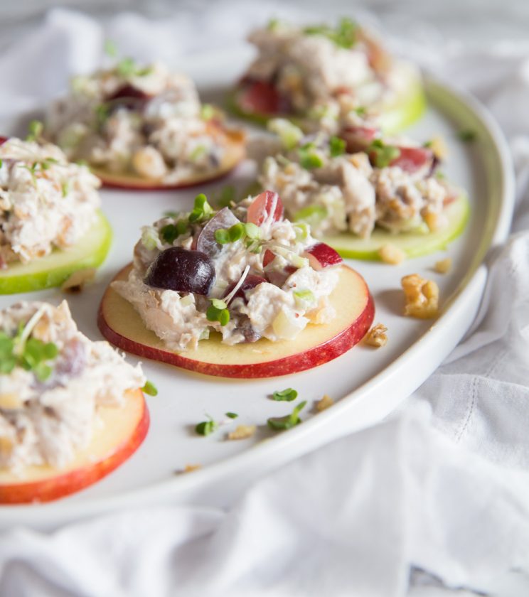 Bocaditos de ensalada de pollo Waldorf servidos en rodajas de manzana con nueces tostadas