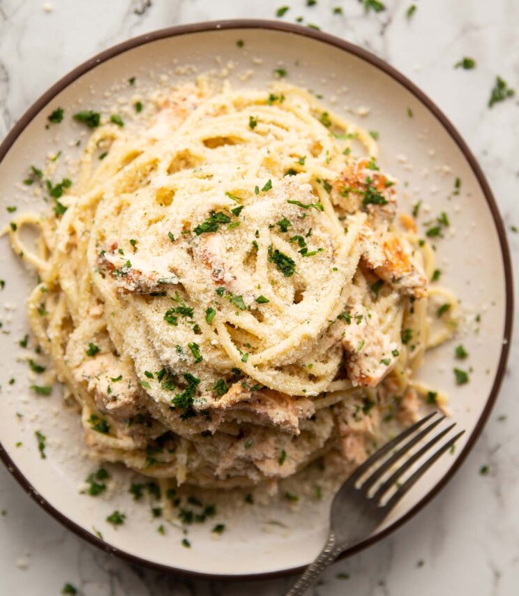 overhead shot of creamy salmon dill pasta on small white plate garnished with parmesan and parsley