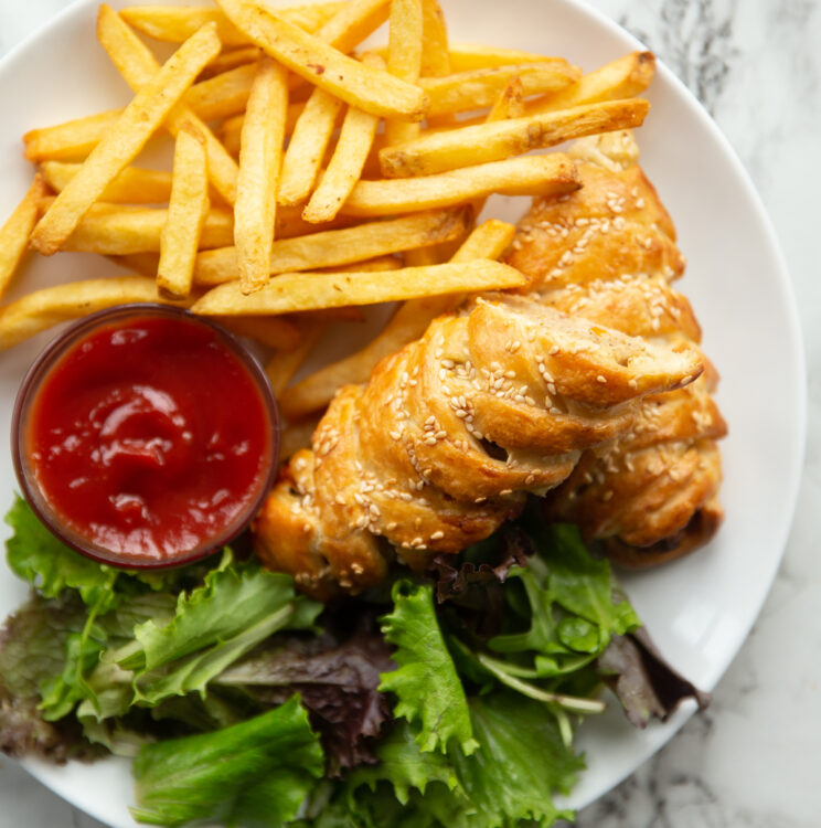 overhead shot of sausage roll on large white plate with fries and salad