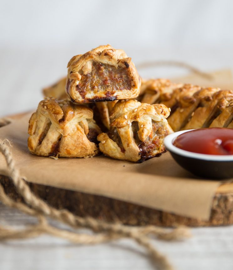 sausage rolls stacked on chopping board with ketchup next to them