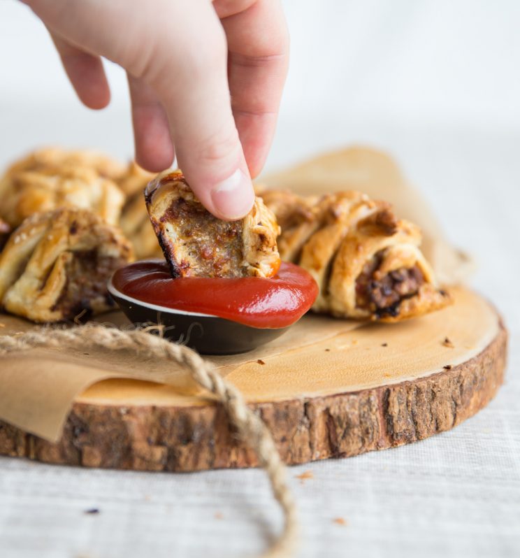 Homemade sausage rolls dipping into ketchup on wooden board