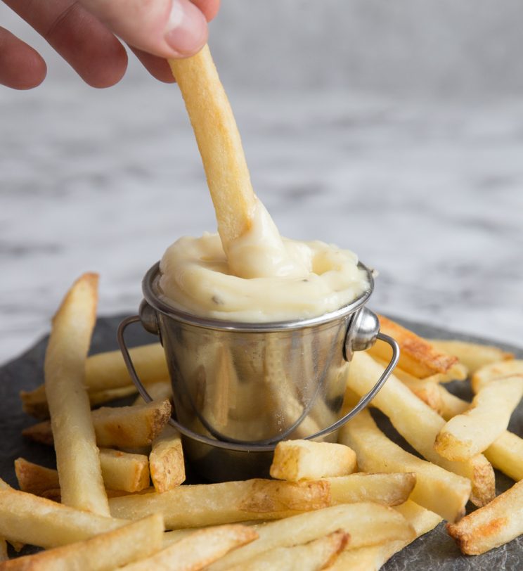 dipping french fry into small pot of aioli surrounded by fries