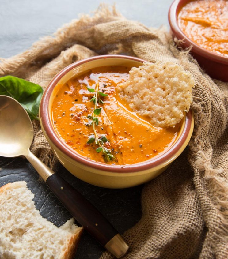 closeup shot of soup in yellow bowl with parmesan chip dunking in 