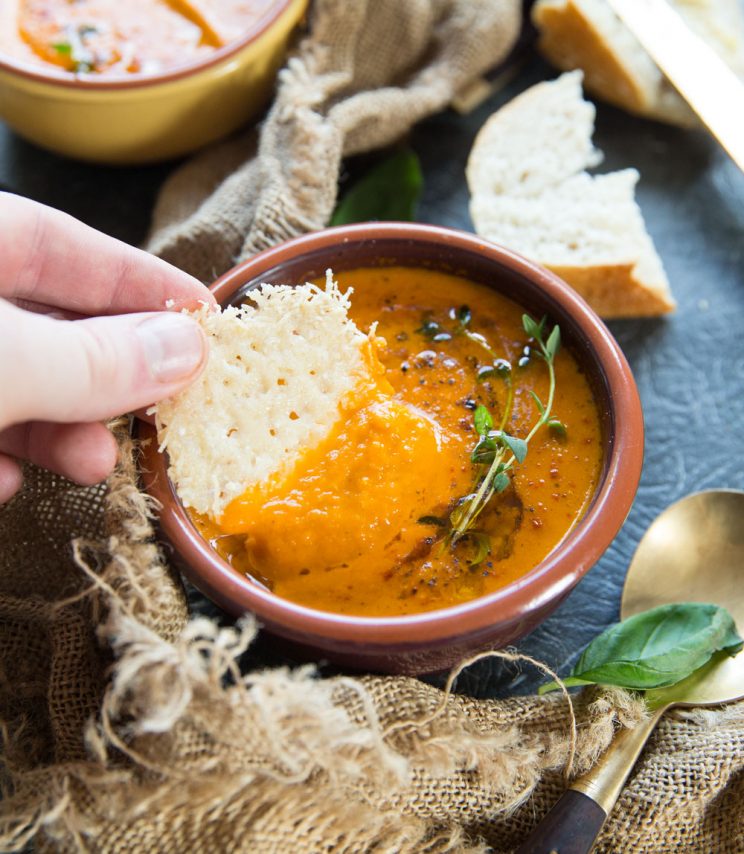 closeup shot of dunking parmesan chip into soup bowl with bread blurred in background