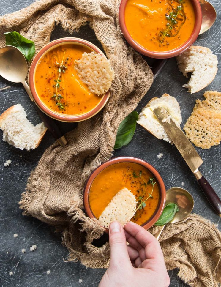 overhead shot of soup bowls with hand dunking parmesan chip into one