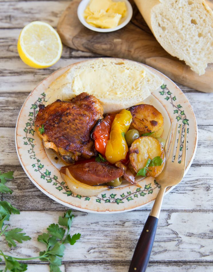 chicken tray bake served on plate with bread and butter with golden fork resting on side