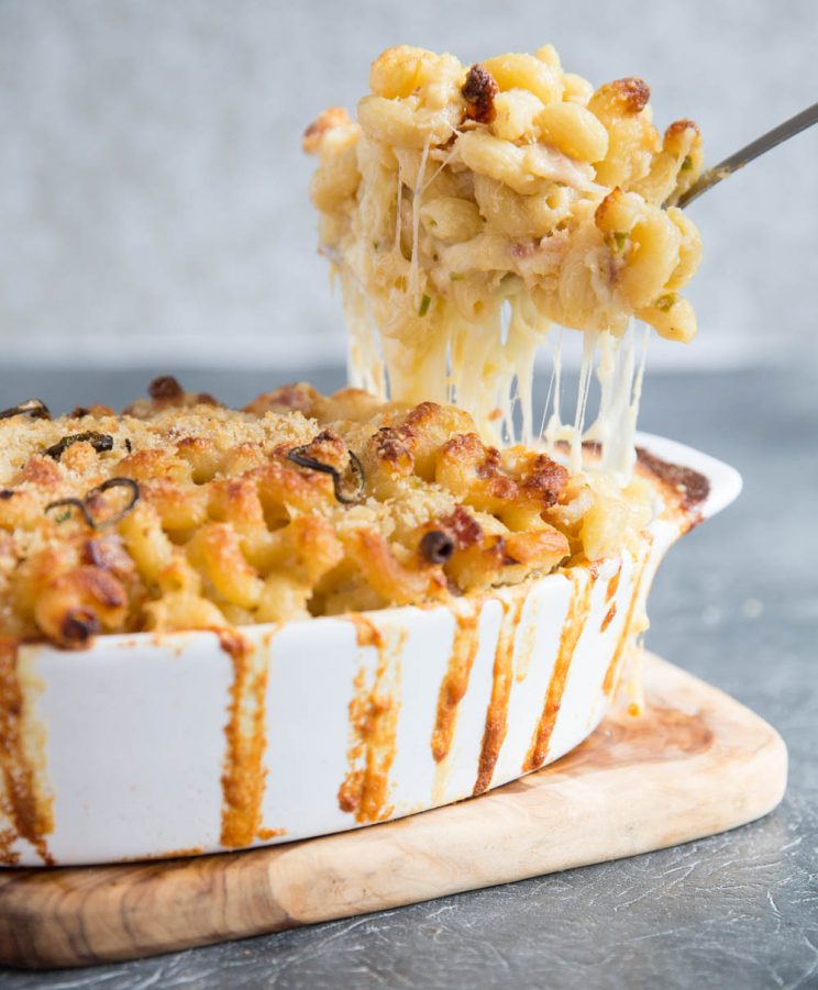 scooping out spicy mac and cheese from baking dish with cheese pull