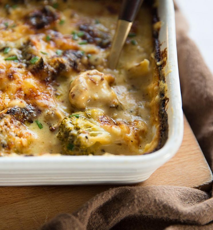 close up shot of gold spoon digging in to white baking dish with broccoli cauliflower cheese