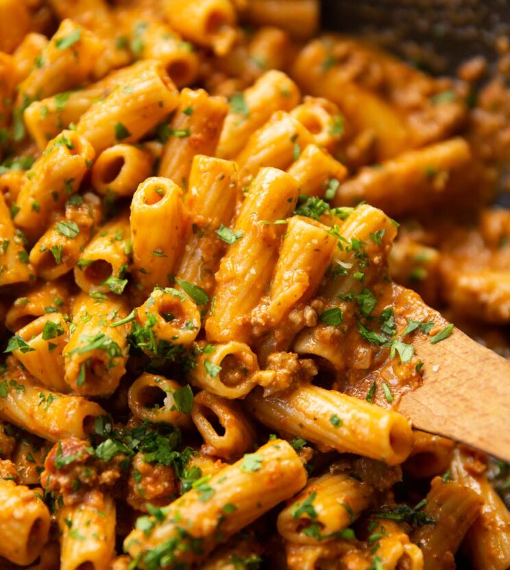 close up shot of wooden spoon digging into skillet of creamy tomato sausage pasta