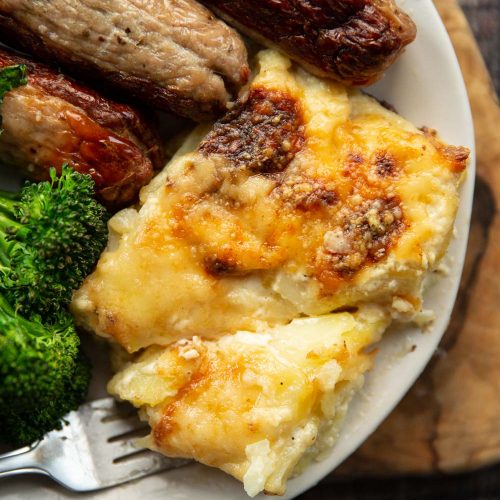 overhead shot of dauphinoise served on plate with sausages and broccolini
