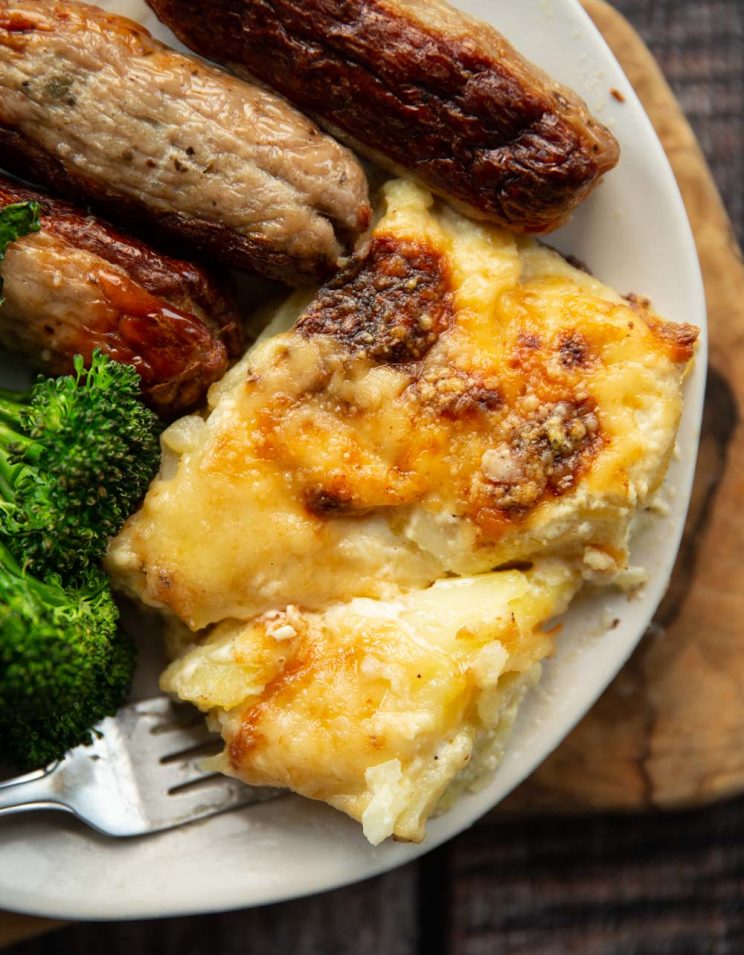 overhead shot of dauphinoise served on plate with sausages and broccolini