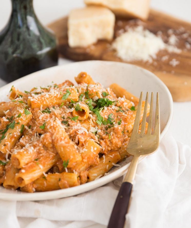 sausage pasta in a long white bowl with parmesan blurred in the background