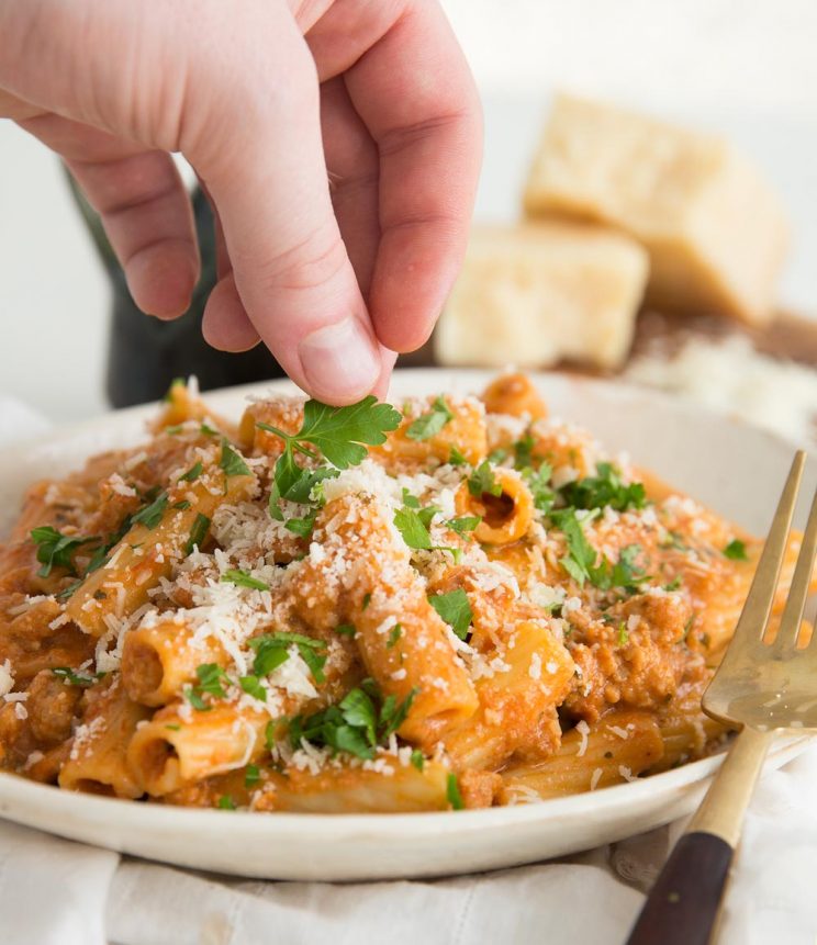 hand placing parsley leaf on plated up pasta garnished with parmesan