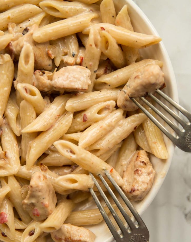 overhead shot of leftover chicken pasta in white bowl with two forks resting on side