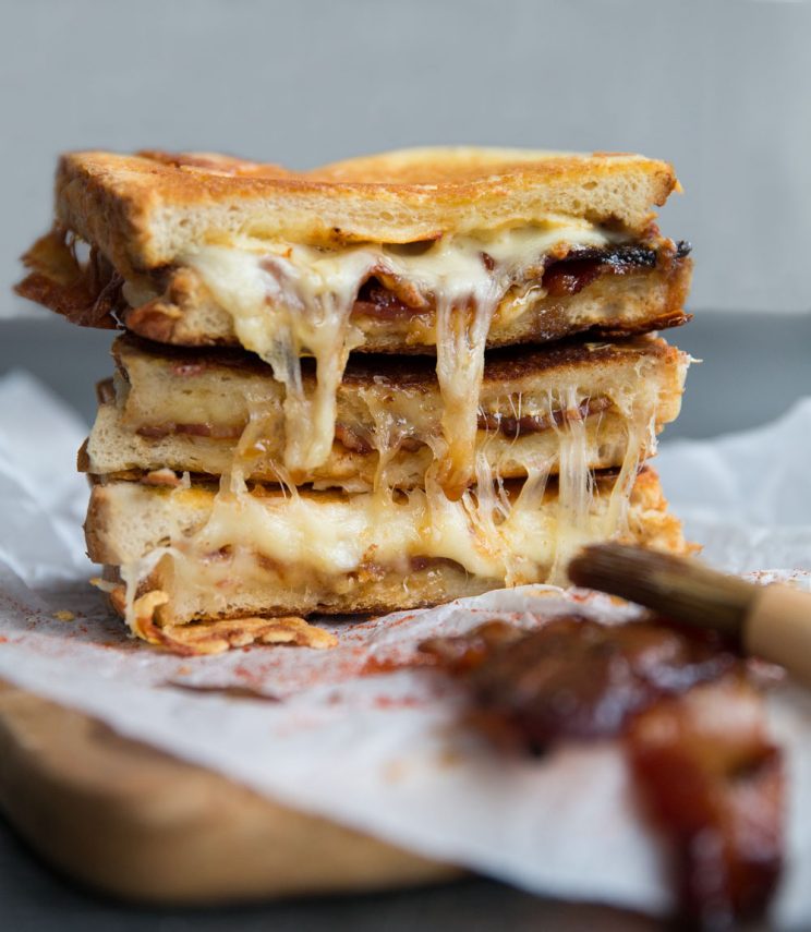 3 grilled cheese sandwiches stacked on each other with maple bacon in the corner