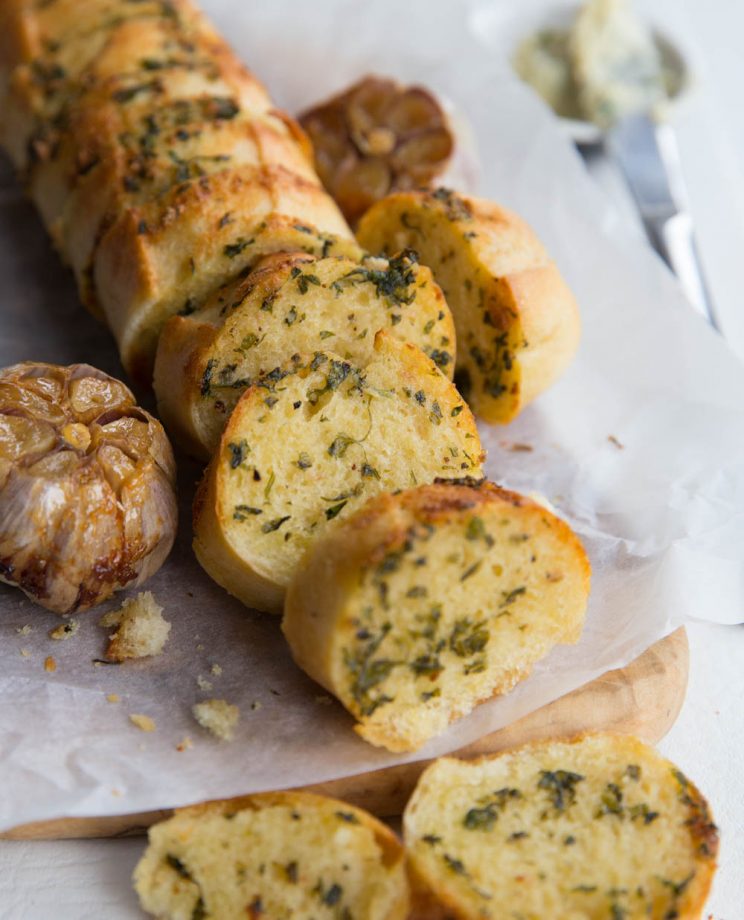 garlic bread served on chopping board next to bulb of roast garlic
