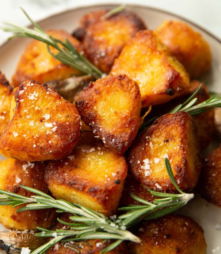 close up shot of roasted potatoes on small white plate garnished with salt and rosemary