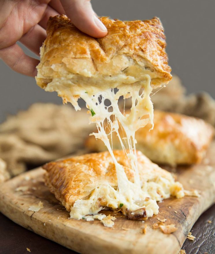 hand pulling half of cheese and onion pasty with cheese dripping out on wooden board