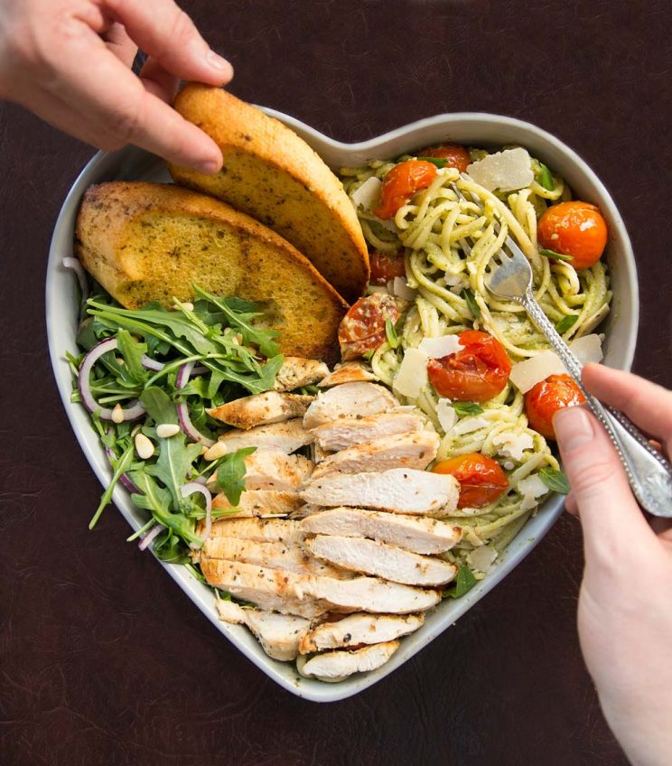 over head shot of pasta served in heart shaped bowls with two hands and forks digging in
