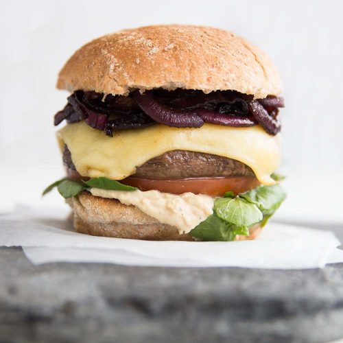 close up shot of Portobello Mushroom Burger with caramelised onions, cheese, hummus, tomato and watercress