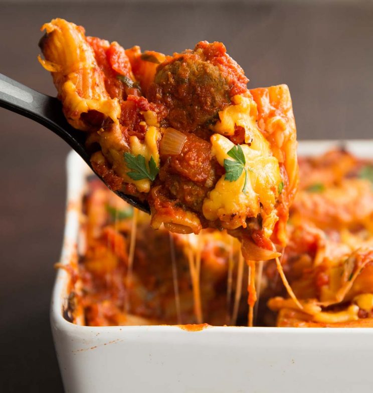 Scooping out meatball and pasta with cheese pouring down spoon
