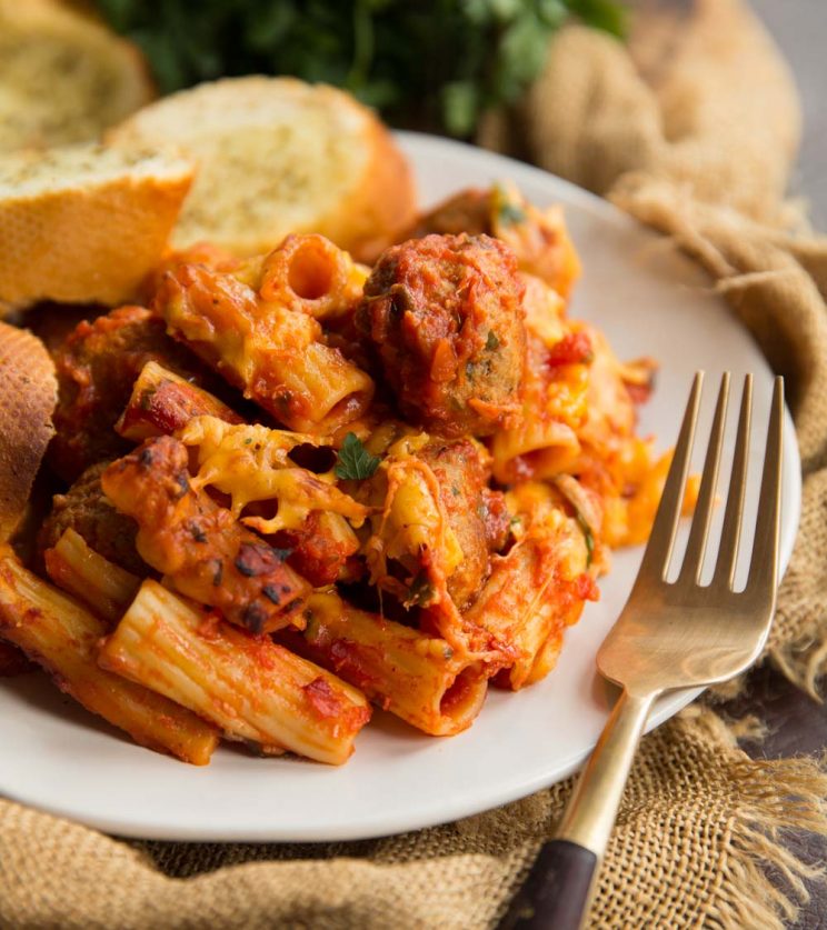 Meatball pasta bake served on a white plate with garlic bread in the background